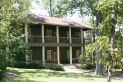 A green two story building with porches and surrounded by trees.