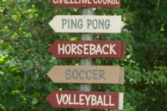 Outdoor wayfinding pole sign pointing the way to various activity areas of camp.