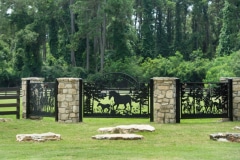 A black iron gate at Camp olympia with ornamental horse scenes in the middle of each section.