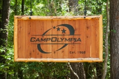 The Camp Olympia logo burned into a hanging wooden sign.