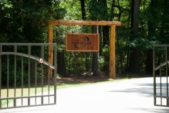 A Camp Olympia wooden sign hanging from the side of a metal entrance gate.