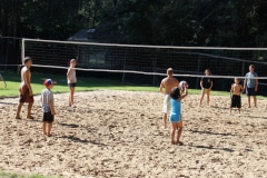 A group of adults and children playing a game of beach volleyball.