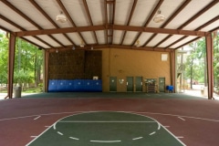 A basketball court and a climbing wall inside of a large outdoor covered structure.