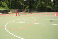 Two tennis courts next to a court with a volleyball net and a basketball hoop.