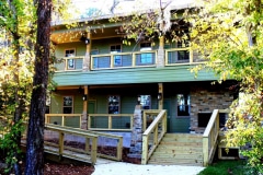 A two story green building with wooden decks, stairs, and ramps.