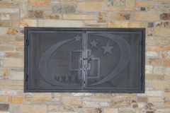 Closed metal doors displaying the Camp Olympia logo on an outdoor fireplace.